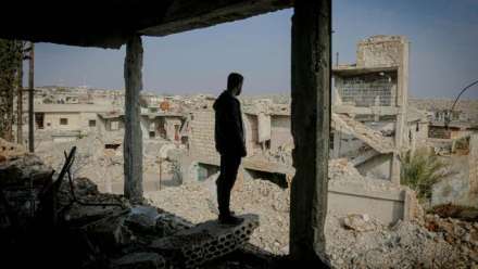 A man stands in the remains of his house that has been bombed looking out of once was a wall at the rubble that his hometown has been reduced to.