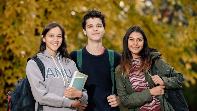 Image of three students with backpacks and books looking at the camera and smiling