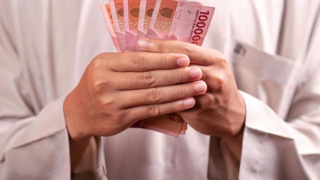 A man dressed in tradition white Muslim attire holds bank notes from South East Asia in his hands
